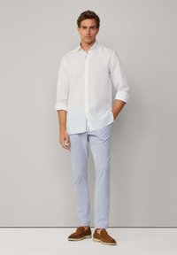 Camisa blanca de botón con mangas remangadas, combinada con pantalones a rayas azul claro y zapatos de ante marrones. Diseño minimalista, textura suave.