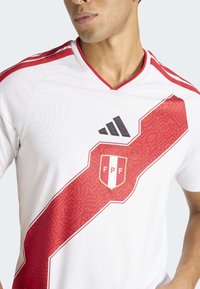 Witte sportshirt met een rode diagonale streep met een gestructureerd patroon. Adidas-logo in zwart en FPF-embleem met rode en witte strepen.