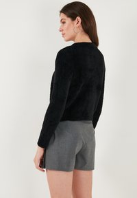 Black fuzzy cropped sweater with long sleeves, paired with gray tailored shorts, featuring a smooth texture and subtle side slit.