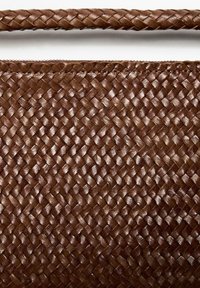 Bruine geweven leren handtas met gevlochten handvat, met gedetailleerde textuur en stiksels.