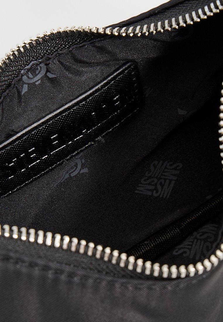 Pochette noire zippée ouverte montrant un intérieur avec un revêtement de marque et une étiquette en cuir noir cousue à l'intérieur.