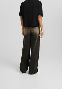 Svart avkortad t-shirt som bärs med vida, urblekta bruna denimjeans. Jeansarna har två bakfickor och en subtil gradienteffekt i färgen.