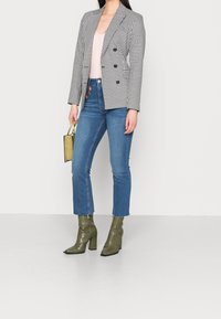 Svart och vit houndstooth-blazer, ljusrosa topp, blå cropped jeans och olivgröna texturerade ankelstövlar. Håller en liten guldfärgad handväska.