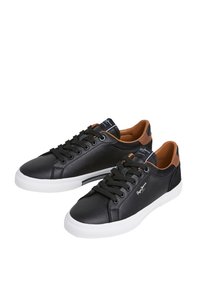 Svarte skinnsneakers med brune detaljer, hvit gummisåle og svarte lisser. Har avrundet tå og merke på siden og tungen.