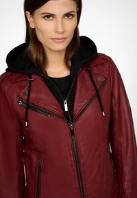 Veste de moto en cuir bordeaux avec une doublure à capuche noire, dotée de zips, de boutons pression et d'une silhouette ajustée.