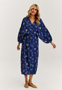 Modrá, středně dlouhá šaty z lehkého materiálu, s abstraktními bílými vzory včetně designů slunce a mušlí. Výstřih do V a elastický pas.