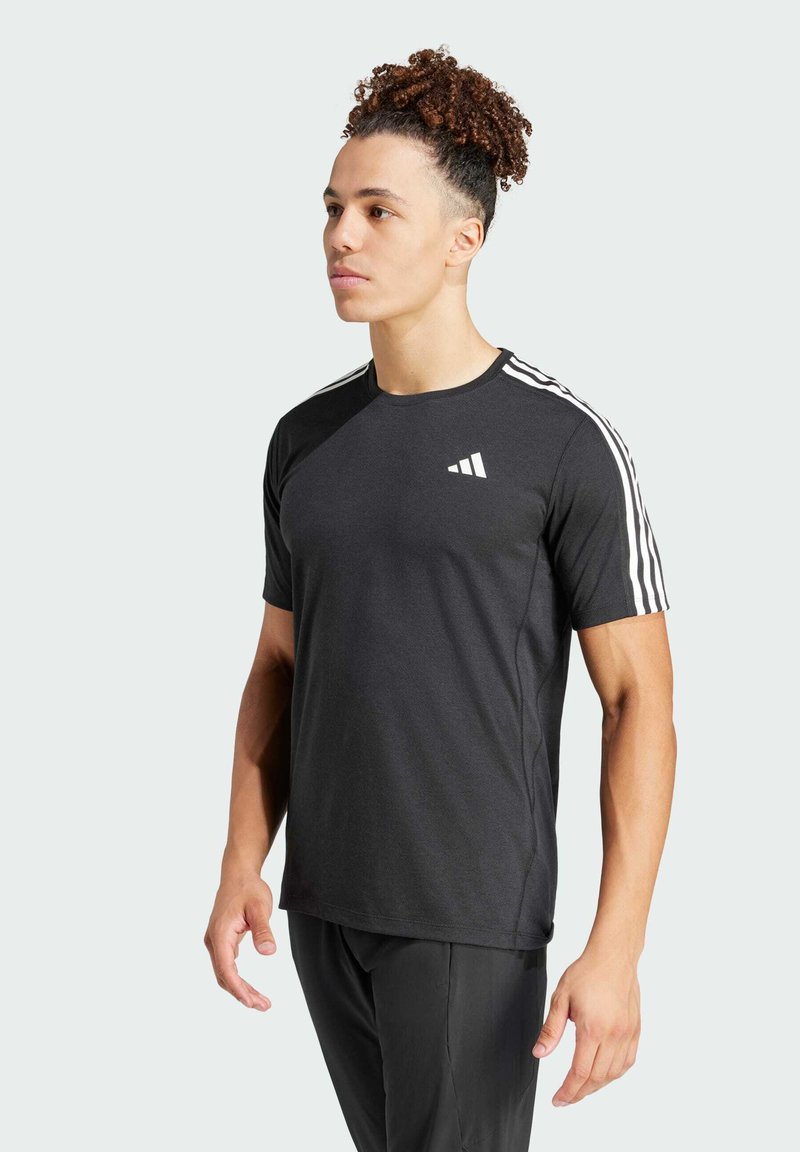 Camiseta deportiva negra de manga corta, con el logo blanco de Adidas en el pecho y tres rayas blancas en los hombros. Textura de tela suave.
