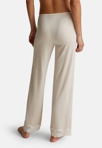 Béžové kalhoty s širokým střihem a texturovaným krajkovým lemem na spodním okraji. Měkký, elastický materiál; má vykrojený pas.