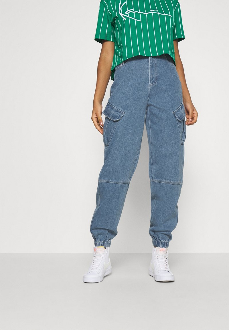 Blå denim cargo-byxor med elastiska muddar och två sidofickor, matchade med en grönrandig crop top med vita accenter.