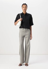 Camicia nera a maniche corte con bottoni, pantaloni dritti grigi chiaro, sandali neri con cinturini e borsa bianca. Tessuto liscio, vestibilità casual.