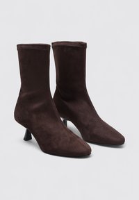 Bottines en daim marron avec des orteils pointus et un talon effilé. Texture lisse et design minimaliste sans quincaillerie ou accents visibles.