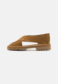 Brune semskede slip-on sko med utskjæringsdesign, robust gummisåle og synlige sømdetaljer langs kanten. Teksturert overflate.