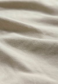 Tela beige clara con textura suave, que presenta arrugas sutiles y un fino patrón tejido. La superficie es blanda y flexible.