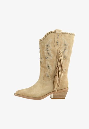 Beige suede mid-calf cowboy boot with decorative stitching, metal studs, fringe detail on side, and stacked wooden heel.