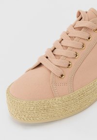 Pink canvas sneaker with a rounded toe, gold-tone eyelets, and a textured jute platform sole. Features flat laces and stitched details.