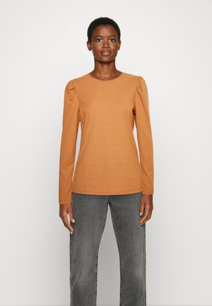 Camisola de mangas longas, canelada, em laranja-acastanhado, com decote redondo e ombros ligeiramente bufantes, combinada com jeans cinzentos. Textura suave.