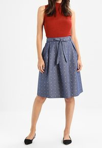 Denim A-linjekjol med små vita hjärtan, med knytmidja och sidofickor. Modellen bär en ribbad röd topp och ballerinas.