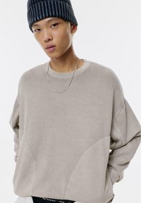 Felpa beige con vestibilità rilassata, scollatura rotonda e maniche oversize. Presenta cuciture a contrasto e pannelli laterali sottili. Collana in catena argentata.