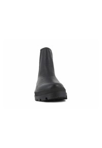 Botín chelsea negro con parte superior de cuero suave, punta redondeada y suela de goma que presenta tacos profundos para un mejor agarre. Diseño minimalista, sin adornos.