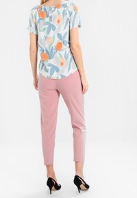 Floral blouse in light blue with orange and green accents, paired with pink tapered pants. Button details at the back, worn with black heels.