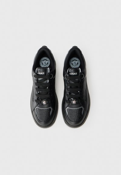 Black leather sneakers with textured side panels, lace-up design, Versace logo, and decorative hardware on the tongue.