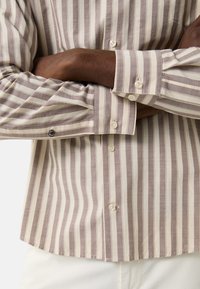 Gestreiftes Hemd in hellem Beige und Braun, mit Knopfverschluss und entspannter Passform. Der Stoff hat eine strukturierte Oberfläche und dekorative Manschettendetails.