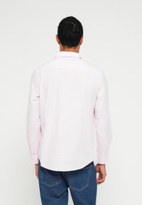Camicia rosa chiaro a maniche lunghe con colletto abbottonato, tessuto liscio, orlo curvo e polsini abbottonati. Indossata con jeans di denim blu.