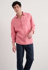 Ljusrosa linneskjorta med knappad krage och en bröstficka, matchad med mörkblå byxor. Mjuk textur och avslappnad passform.