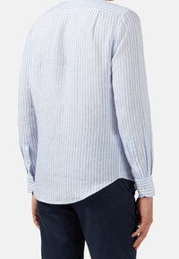 Jasnoniebieska, w paski, długa koszula z długim rękawem, wykonana z lekkiego materiału. Posiada mankiety zapinane na guziki i zaokrąglony dół.