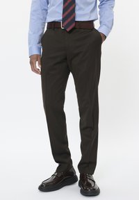 Ciemnobrązowe, dopasowane spodnie o gładkiej fakturze, zestawione z jasno-niebieską koszulą na guziki i granatowym krawatem w czerwone paski. Brązowe skórzane buty.