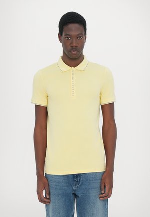 Polo shirt giallo in cotone, con un taglio slim, maniche corte e colletto con bordo a contrasto. Include un logo lungo la patta.