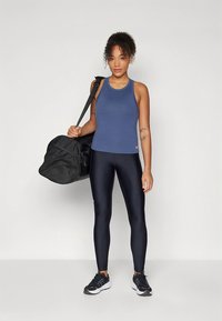 Conjunto de ropa deportiva que incluye una camiseta sin mangas ajustada de color azul oscuro y leggings negros. Bolsa de gimnasio negra colgada de un hombro, con zapatillas deportivas.