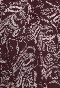 Burgundy tyg med intrikata vita och rosa blommönster som har abstrakta bladmönster och känsliga detaljer genom hela.