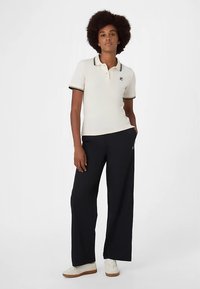 Valkoinen pikeepaita mustalla reunuksella, yhdistetty löysälahkeisiin tummansinisiin housuihin. Valkoiset tennarit, joissa on rento mutta ryhdikäs muotoilu.