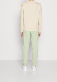 Ljusbeige sweatshirt med rund halsringning och ribbade ärmslut, i kombination med mintgröna joggers med elastiska ärmslut, bärs med vita sneakers.