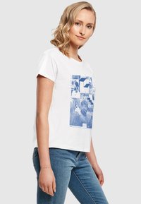 Hvid bomulds t-shirt med korte ærmer, prydet med et blåt grafisk print af forskellige billeder og tekst på forsiden.