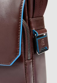 Braune Ledertasche mit blauen Akzentstreifen, silbernem Reißverschluss und schwarzem Metallverschluss. Glatte Textur mit detaillierter Naht.