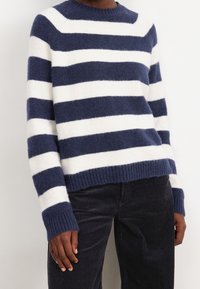 Pull rayé en tricot avec des rayures alternées bleu marine et blanches, col rond et poignets et ourlet côtelés. Tissu doux et texturé.