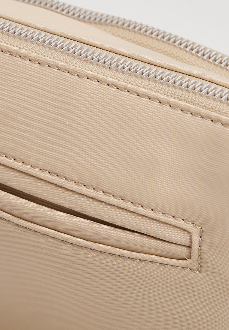 Beige Stoffbeutel mit silbernem Reißverschluss, auf der Vorderseite mit einer flachen Tasche. Glatte Textur und sauberes Nähdetail sichtbar.
