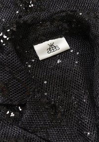 Țesătură din fibră cu paiete negre, având o textură din plasă, având o etichetă albă cu logo negru. Detaliul de aproape evidențiază paiete mici, reflexive.