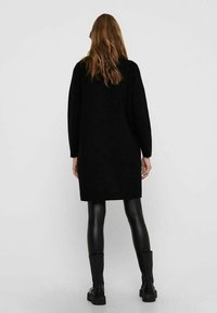 Černé svetr šaty do kolen s dlouhými rukávy, vyrobené z texturované tkaniny. Nosené s černými legínami z umělé kůže a kotníkovými botami.