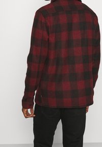 Rood-zwart geruit flanellen overhemd met knoopmanchet, losse pasvorm, zachte textuur en een kraag, gezien vanaf de achterkant.