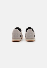 Lys grå semsket lær sneakers med sorte accenter, teksturert hæl, perforerte paneler og en såle av gummirubber. Bakfra viser den to-farget design.