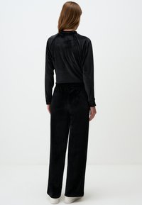 Tuta in velluto nero con top a maniche lunghe e pantaloni larghi. Tessuto morbido, cintura elastica e design elegante.
