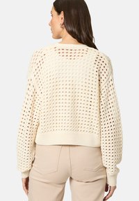 Crème gebreide trui met een losse, boxy pasvorm en een open, lattice-achtige structuur. Heeft ribbels aan de mouwen en onderkant, ontworpen voor een relaxte stijl.