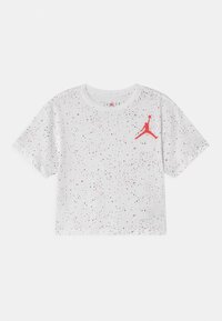 Biała krótka koszulka z czarnymi i czerwonymi plamkami, z czerwonym logo Jumpman na lewej górnej części klatki piersiowej.