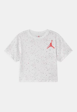 T-shirt cropped blanc avec des taches noires et rouges, présentant un logo Jumpman rouge sur le coin supérieur gauche de la poitrine.
