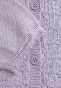 Lila stickad cardigan med ett texturerat mönster, med en ribbad nederkant och dekorativa lila knappar. Mjuk material.