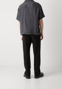 Camisa de manga corta, de color gris oscuro, hecha de una tela suave, con corte recto y detalle en el yugo trasero; combinada con pantalones y zapatos negros.