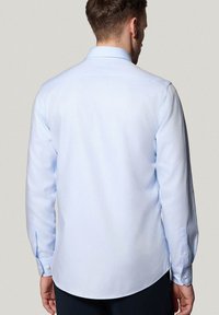 Jasnoniebieska koszula z długim rękawem z kołnierzykiem zapinanym na guziki, o gładkiej fakturze i mankietach zapinanych na jeden guzik; regularny krój z zaokrąglonym dolnym brzegiem.